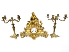 A 19th century French gilt metal figural mantel clock, with a pair of similar candlesticks,