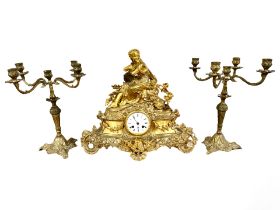 A 19th century French gilt metal figural mantel clock, with a pair of similar candlesticks,