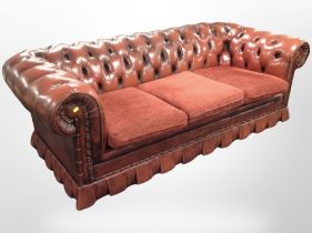 An oxblood buttoned leather Chesterfield three-seater settee with fabric cushions,