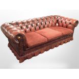 An oxblood buttoned leather Chesterfield three-seater settee with fabric cushions,