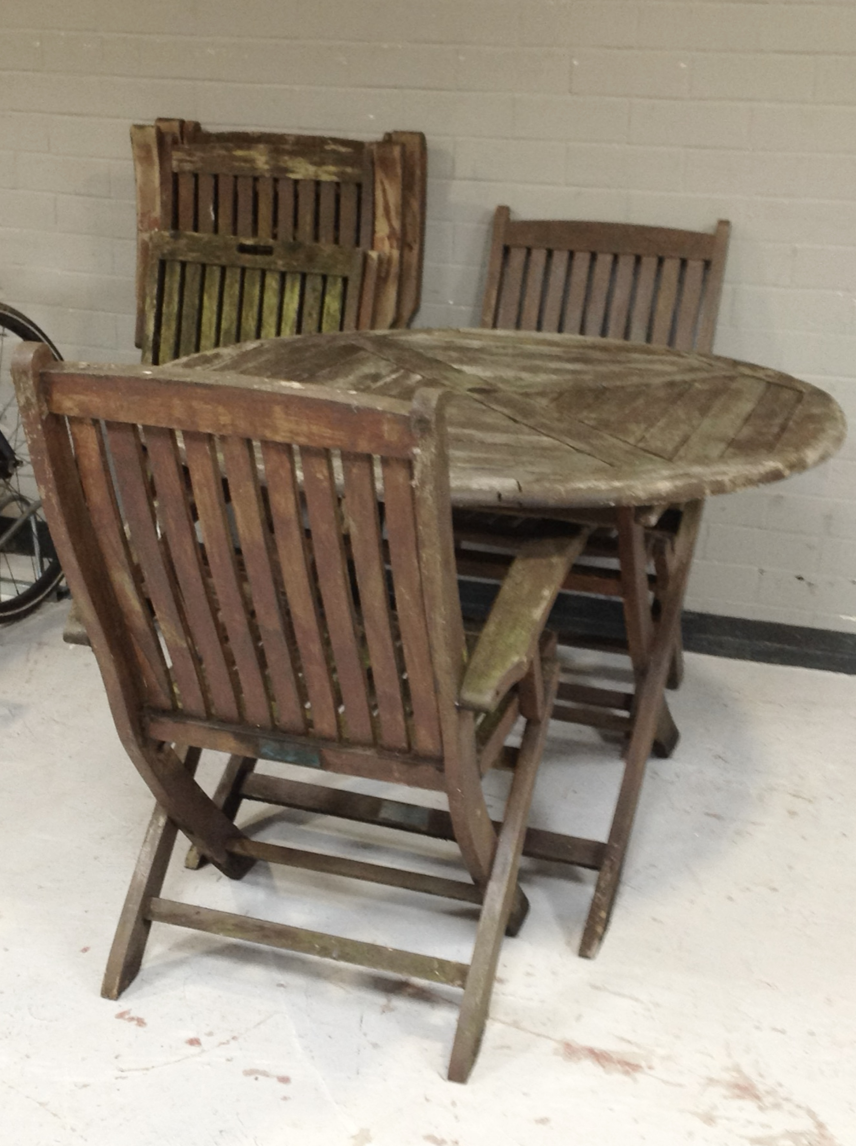 A weathered teak circular folding garden table, diameter 110cm, and a set of four folding armchairs.