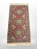 An Afghan/Caucasian rug on red ground, 117cm x 55cm.