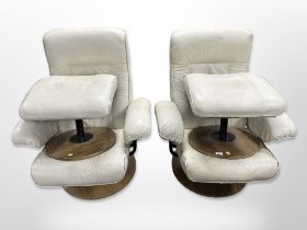 A pair of cream stitched leather armchairs on circular wooden bases,