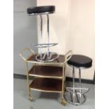 A pair of contemporary chrome and vinyl stools and a three tier serving trolley