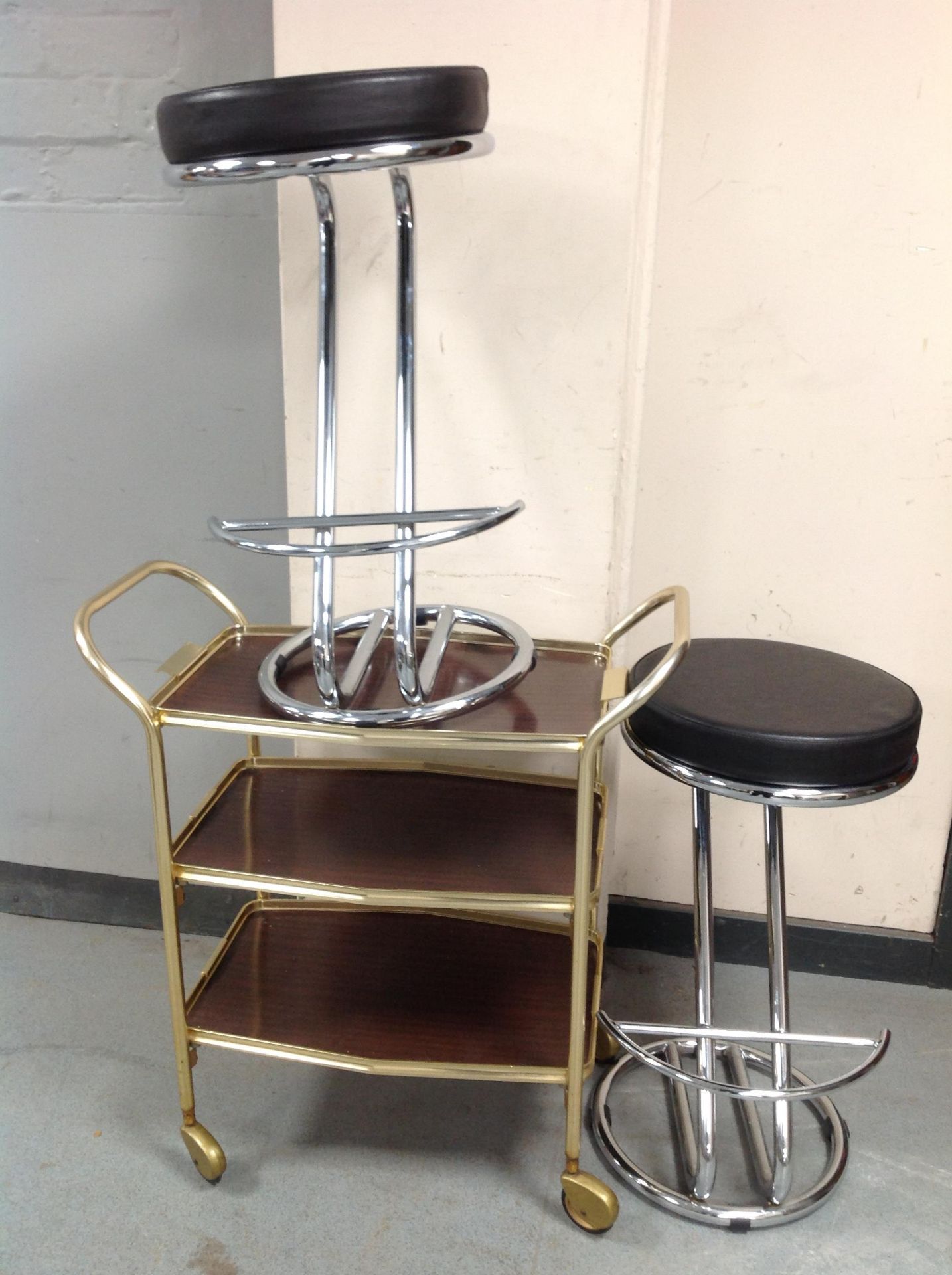 A pair of contemporary chrome and vinyl stools and a three tier serving trolley