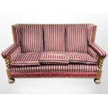 An early 20th century carved oak framed three-seater settee in striped upholstery,