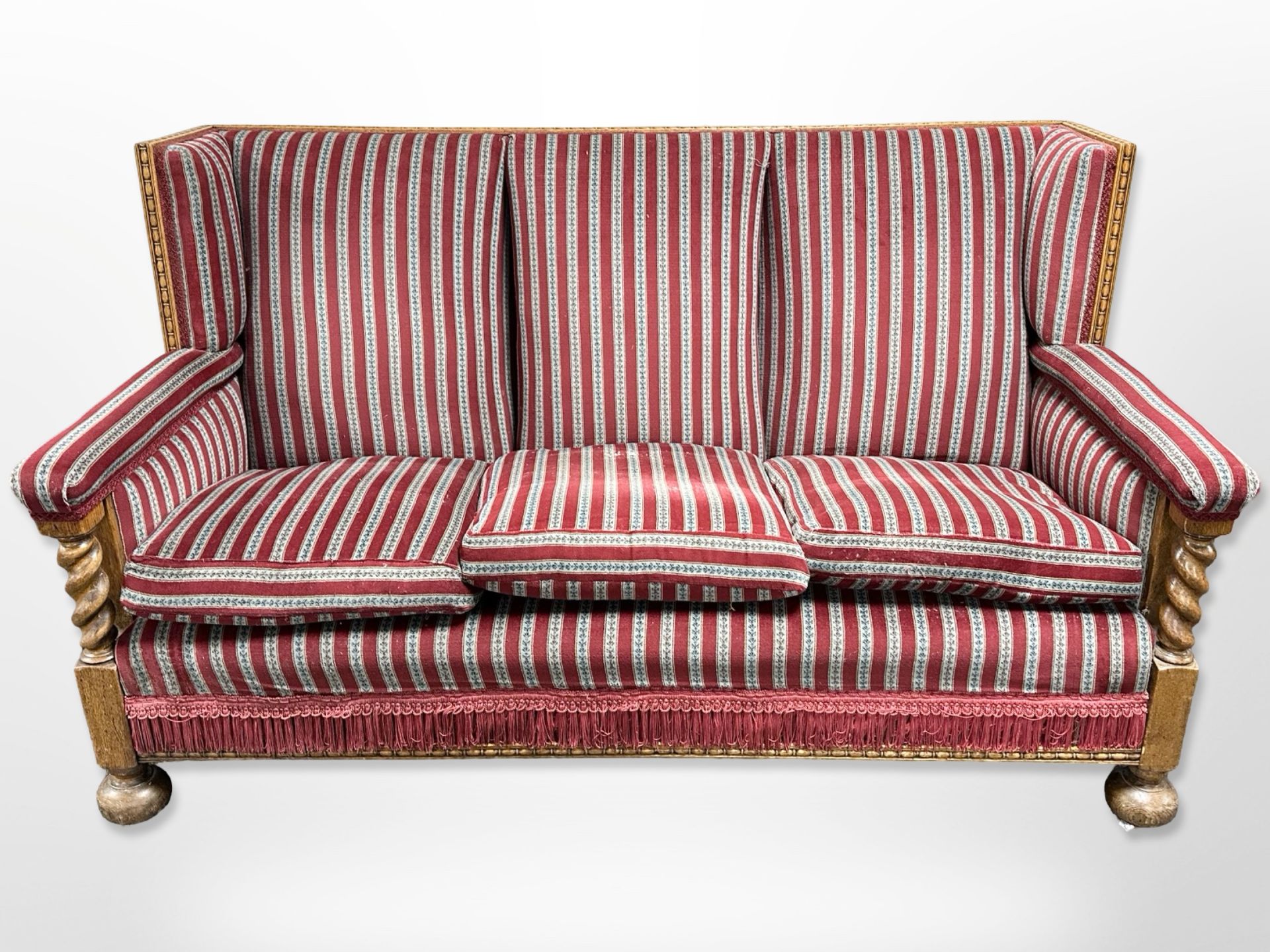 An early 20th century carved oak framed three-seater settee in striped upholstery,