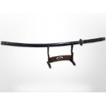 A 20th-century Japanese katana in lacquered scabbard on wooden sword stand, overall length 113cm.