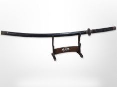 A 20th-century Japanese katana in lacquered scabbard on wooden sword stand, overall length 113cm.