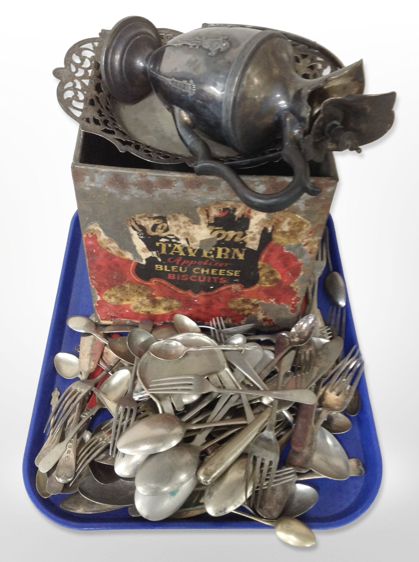 An antique biscuit tin, silver-plated swing-handled basket and jug, and a quantity of cutlery.