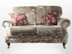 A contemporary Victorian style two seater settee in plush fabric with two cushions raised on brass