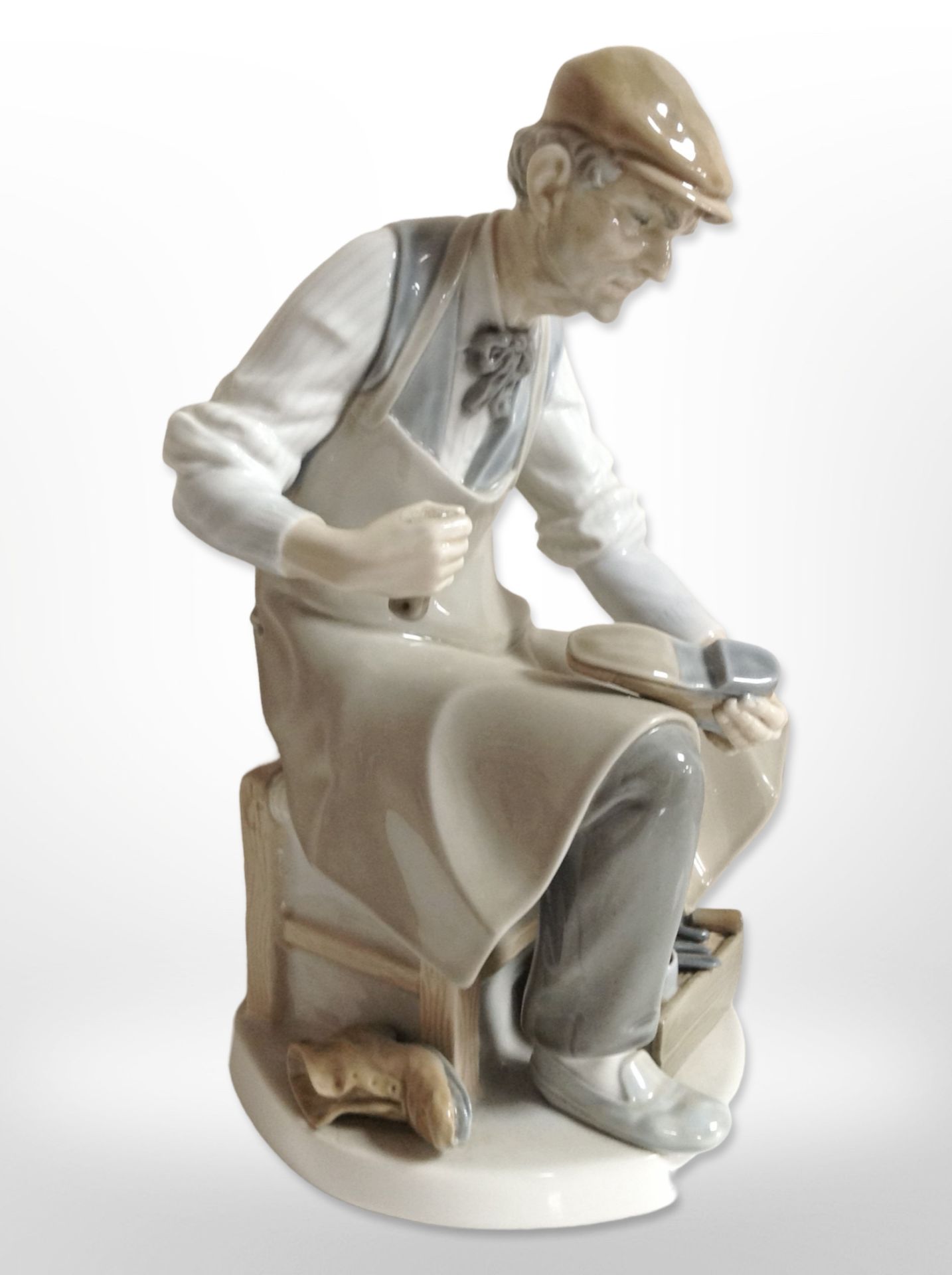 A Lladró figure of a cobbler, and a further figure of a lady reading from a book.
