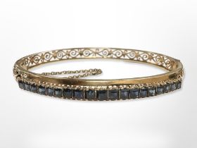 A yellow gold bangle set with sapphires, 5.5 cm x 6 cm, tested as 14ct gold.