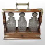 An oak and silver plate-mounted tantalus containing three decanters, width 37cm.