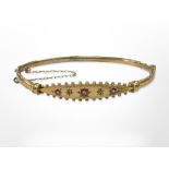An antique 9ct yellow gold bangle set with three rubies and two small diamonds,