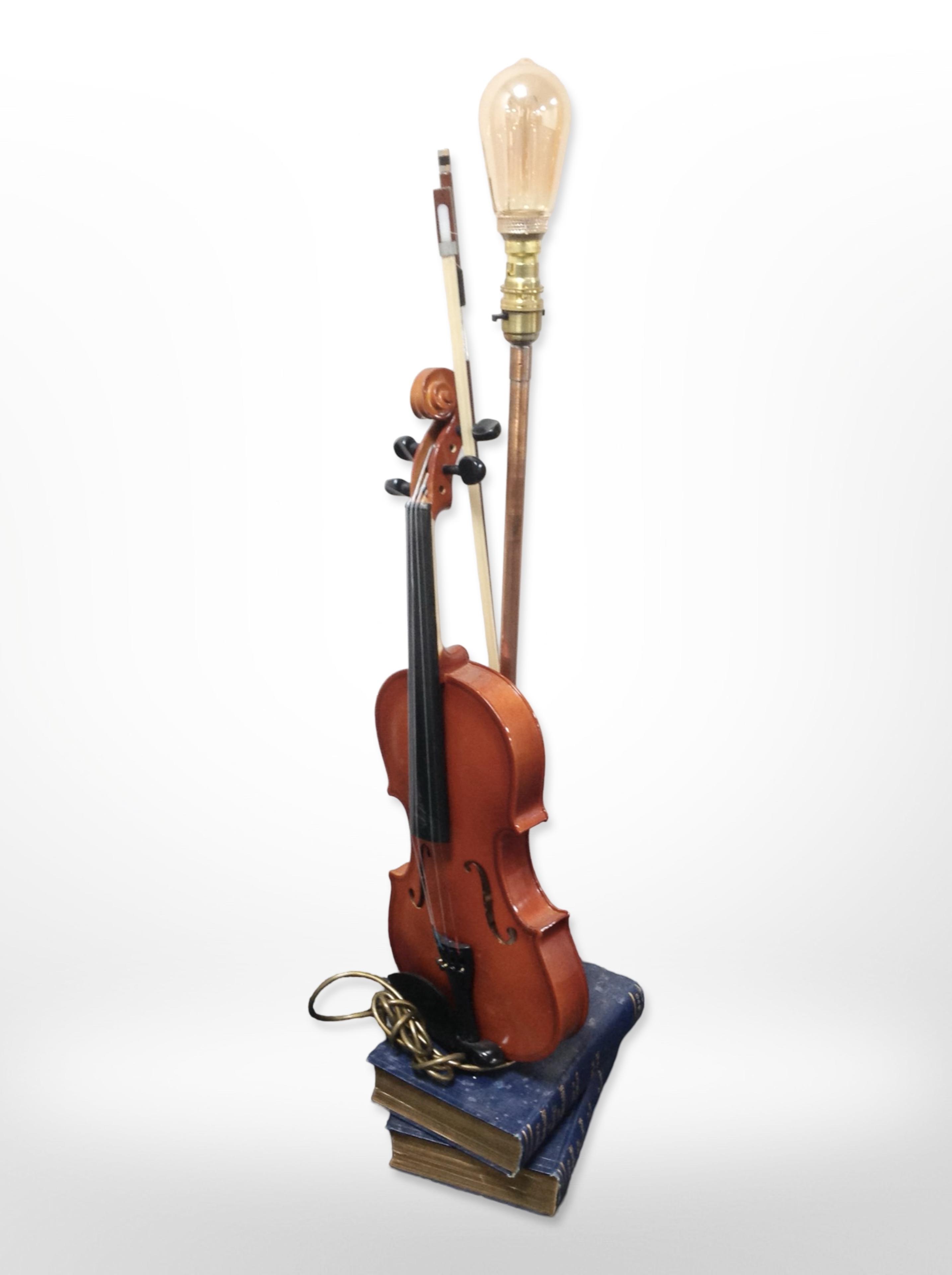 A contemporary table lamp in the form of a violin on top of a stack of books,