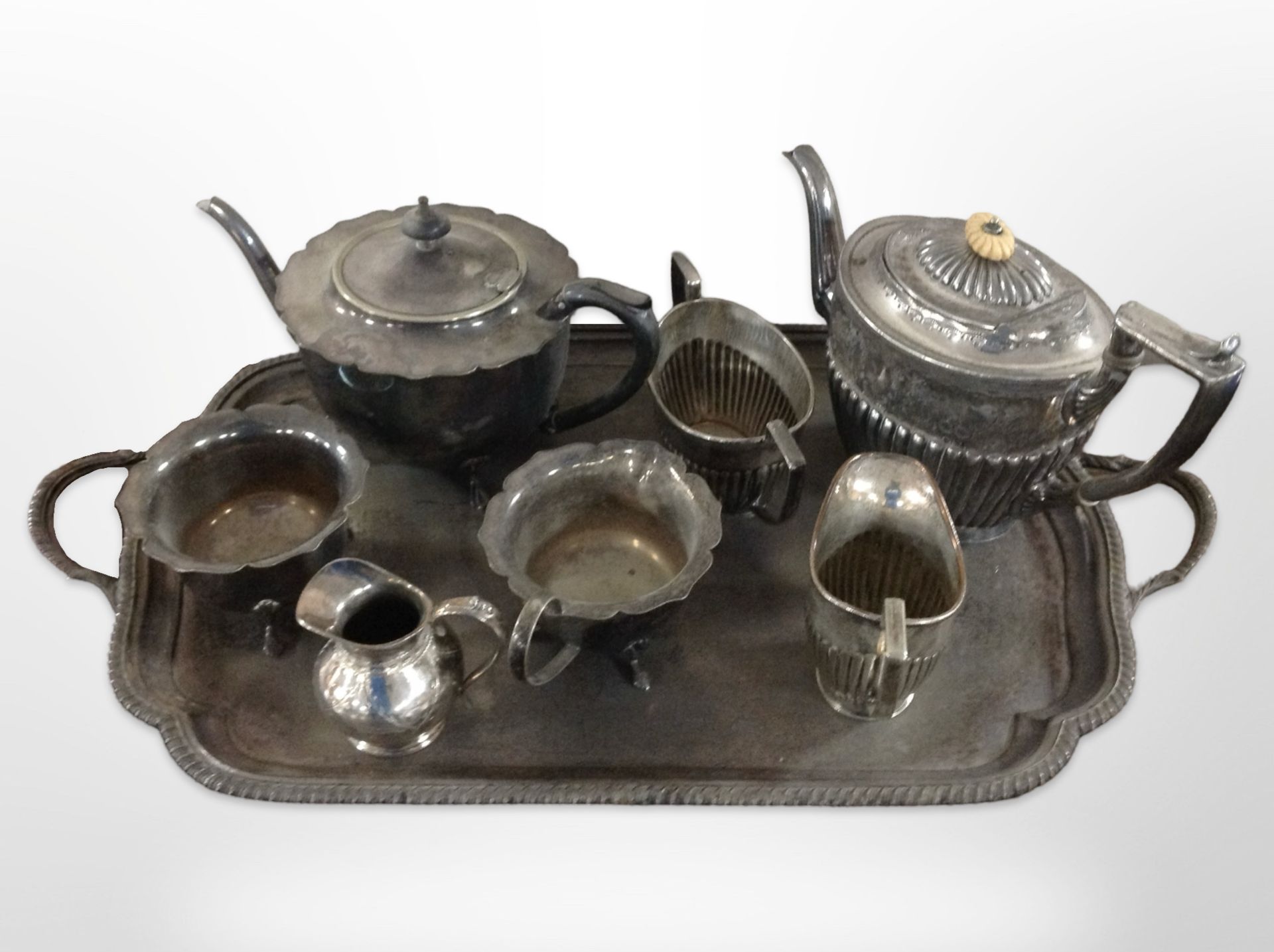 A silver plated twin handled serving tray containing assorted tea wares