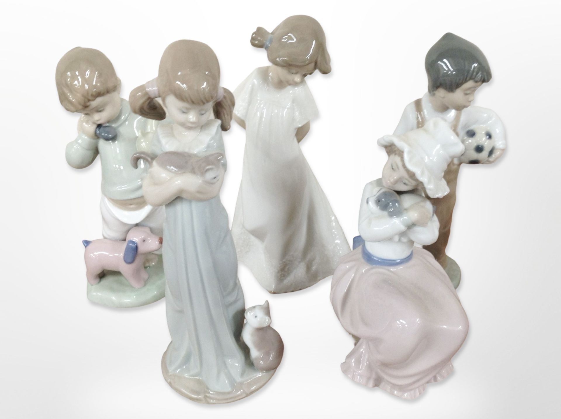 A Lladró figure of a girl holding a kitten, No. 5743, and four further Nao figures of children.