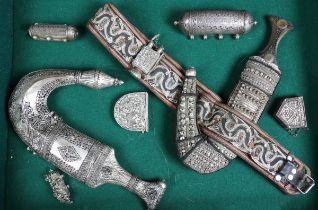 Two mid-20th century Omani jambiya daggers, each with silver metal mounts, and two hirz or amulet