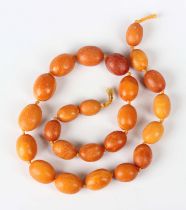 A single row necklace of twenty-four graduated oval opaque mottled butterscotch coloured amber