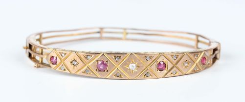 A late Victorian 9ct gold, ruby and diamond oval hinged bangle, the front mounted with four