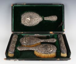 An Edwardian silver six-piece dressing table set, embossed with flowers and foliate scrolls,