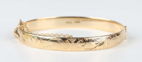 A 9ct gold oval hinged bangle with scroll engraved decoration, on a snap clasp, fitted with a safety