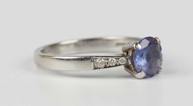 A platinum, tanzanite and diamond ring, claw set with the circular cut tanzanite between diamond