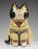 A Joan de Bethel Rye Pottery cat, typically modelled seated, wearing a beige coat and red and