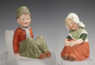 A pair of Continental bisque porcelain figures of seated Dutch children, circa 1900, he before an