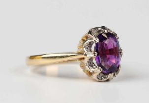 An 18ct gold, amethyst and diamond ring, claw set with the oval cut amethyst within a diamond set