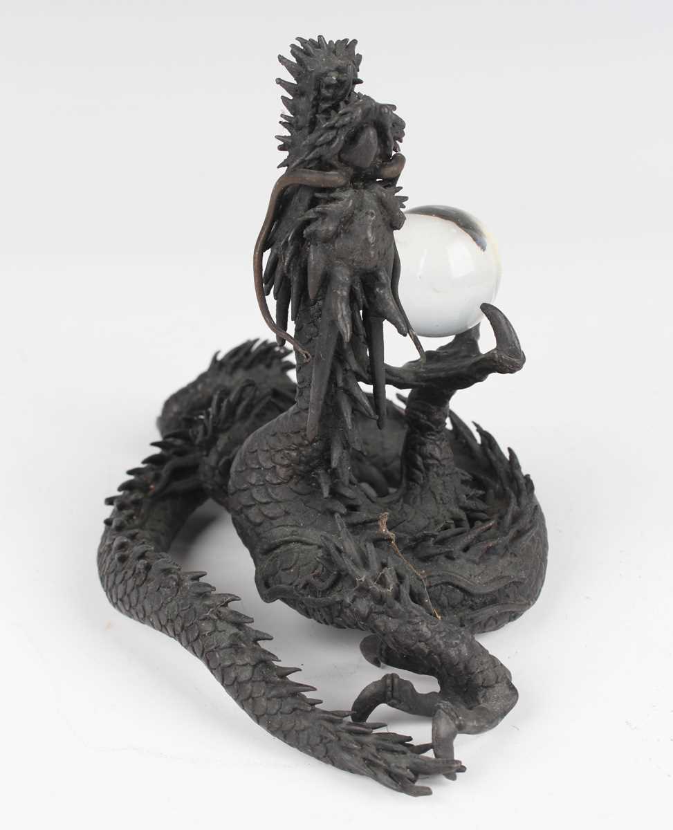 A Japanese cast bronze figure of a dragon, 20th century, modelled in a coiled pose holding a