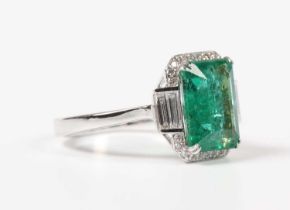 A white gold, treated emerald and diamond ring, claw set with a cut cornered rectangular step cut