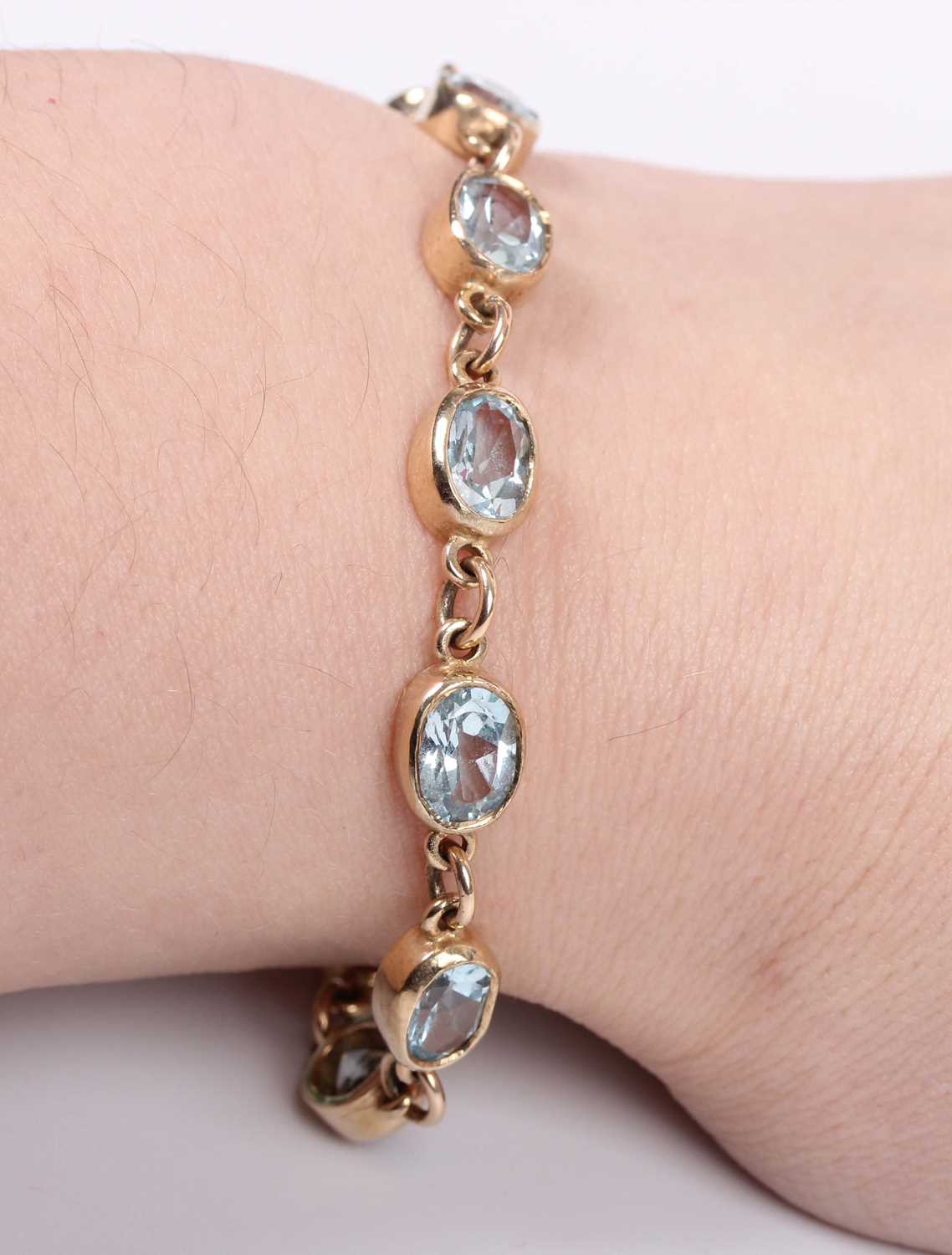 A gold and treated blue topaz bracelet, collet set with a row of oval cut treated blue topazes, on a - Image 2 of 2