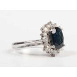 A white gold, sapphire and diamond oval cluster ring, claw set with the oval cut sapphire within a