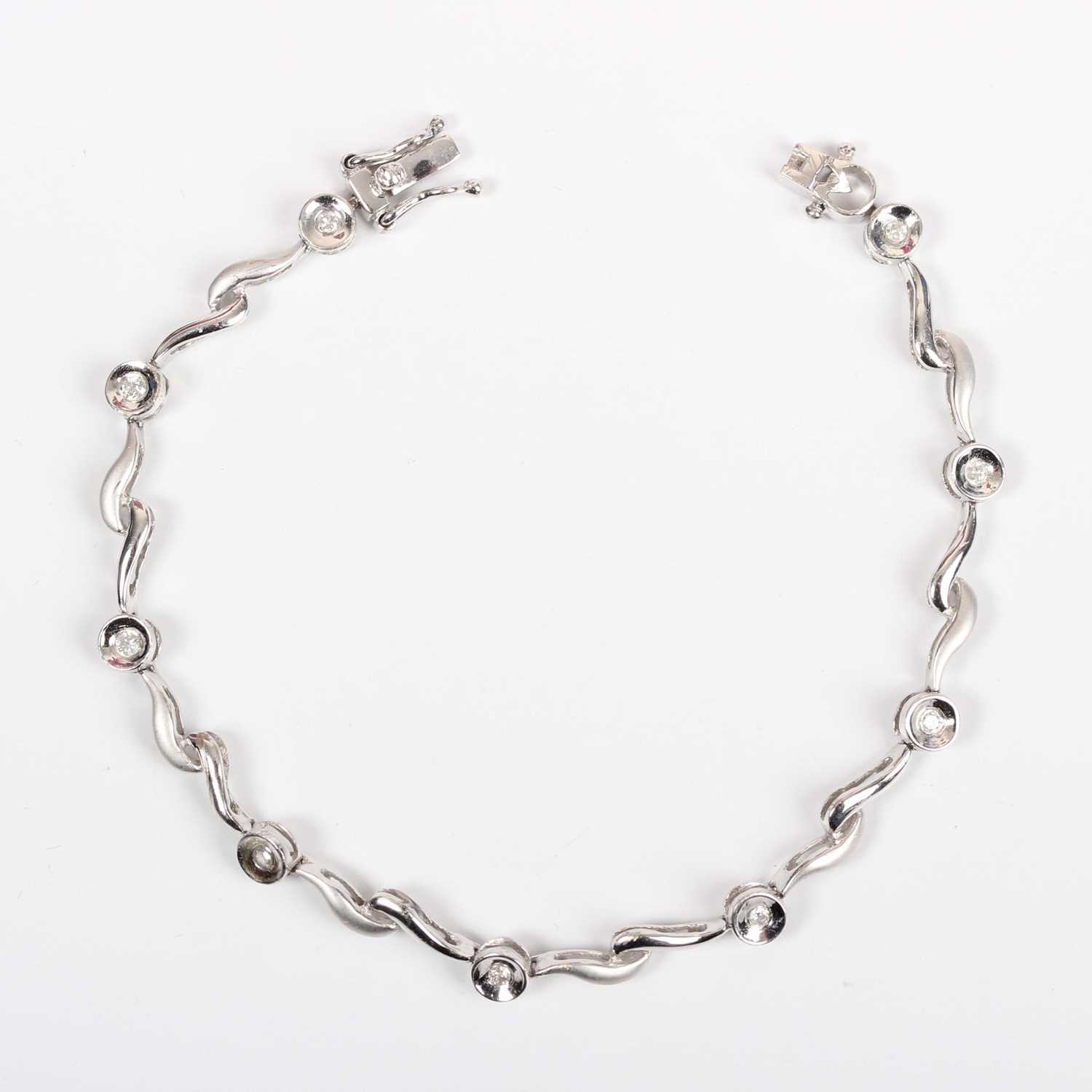 A white gold and diamond bracelet, mounted with a row of nine circular cut diamonds between scroll