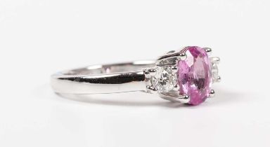 An 18ct white gold, treated pink sapphire and diamond ring, claw set with the oval cut treated