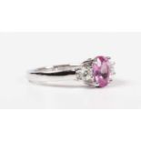 An 18ct white gold, treated pink sapphire and diamond ring, claw set with the oval cut treated