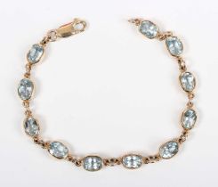 A gold and treated blue topaz bracelet, collet set with a row of oval cut treated blue topazes, on a