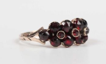 A gold and Bohemian garnet ring, mounted with three small faceted garnets within a surround of ten