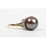 An 18ct gold ring, mounted with a large grey tinted cultured pearl between two rows of three