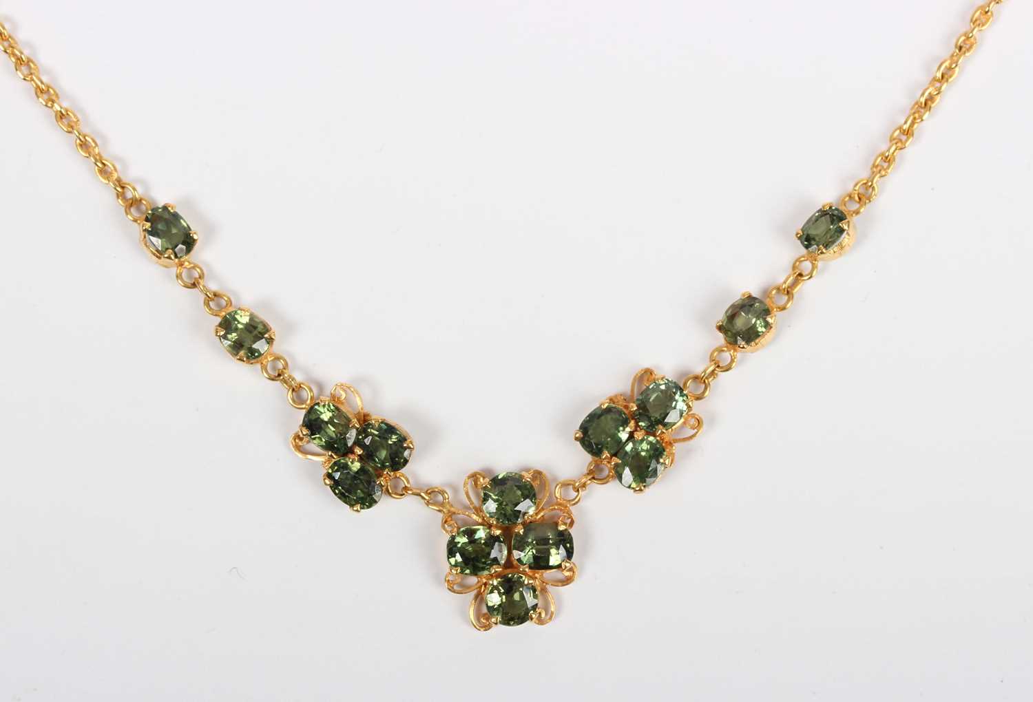 A gold and green sapphire necklace, the front in a scrolling design mounted with oval cut green