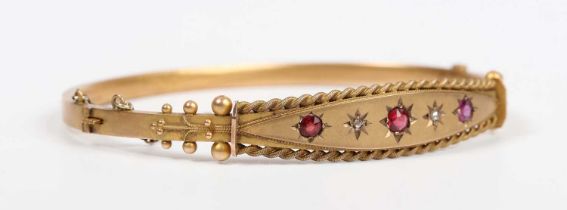 An Edwardian 9ct gold, diamond, ruby and red gem set oval hinged bangle with applied ropetwist and