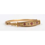 An Edwardian 9ct gold, diamond, ruby and red gem set oval hinged bangle with applied ropetwist and