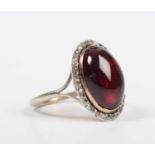 A carbuncle garnet and diamond ring, mounted with the oval carbuncle garnet within a surround of