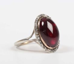 A carbuncle garnet and diamond ring, mounted with the oval carbuncle garnet within a surround of
