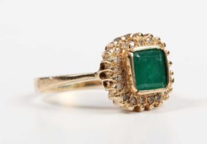 A gold, emerald and diamond cluster ring, collet set with the cut cornered square cut emerald within