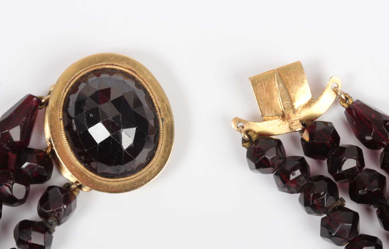 A three row necklace of faceted garnet and red paste beads, on a gold and faceted garnet oval clasp, - Image 2 of 4