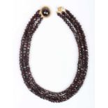 A three row necklace of faceted garnet and red paste beads, on a gold and faceted garnet oval clasp,