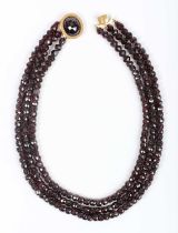 A three row necklace of faceted garnet and red paste beads, on a gold and faceted garnet oval clasp,